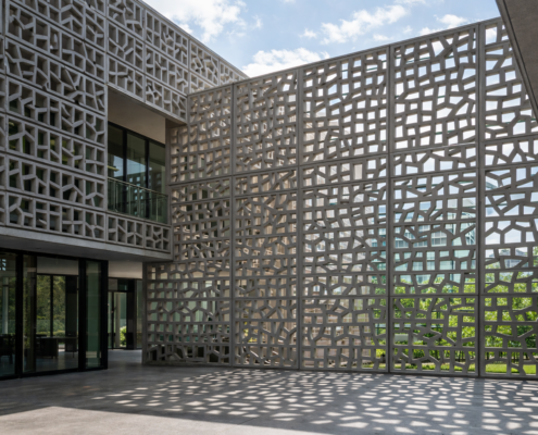 Façade contemporaine avec résille de béton ajourée, motifs géométriques et ombres portées, ambiance lumineuse et élégante